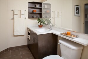 Un baño moderno con un lavabo blanco, armarios de madera oscura, una planta en maceta y un espejo sobre el lavabo.
