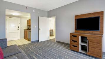 A modern living room with a flat-screen TV, wooden entertainment unit, grey carpet, and a grey sofa.