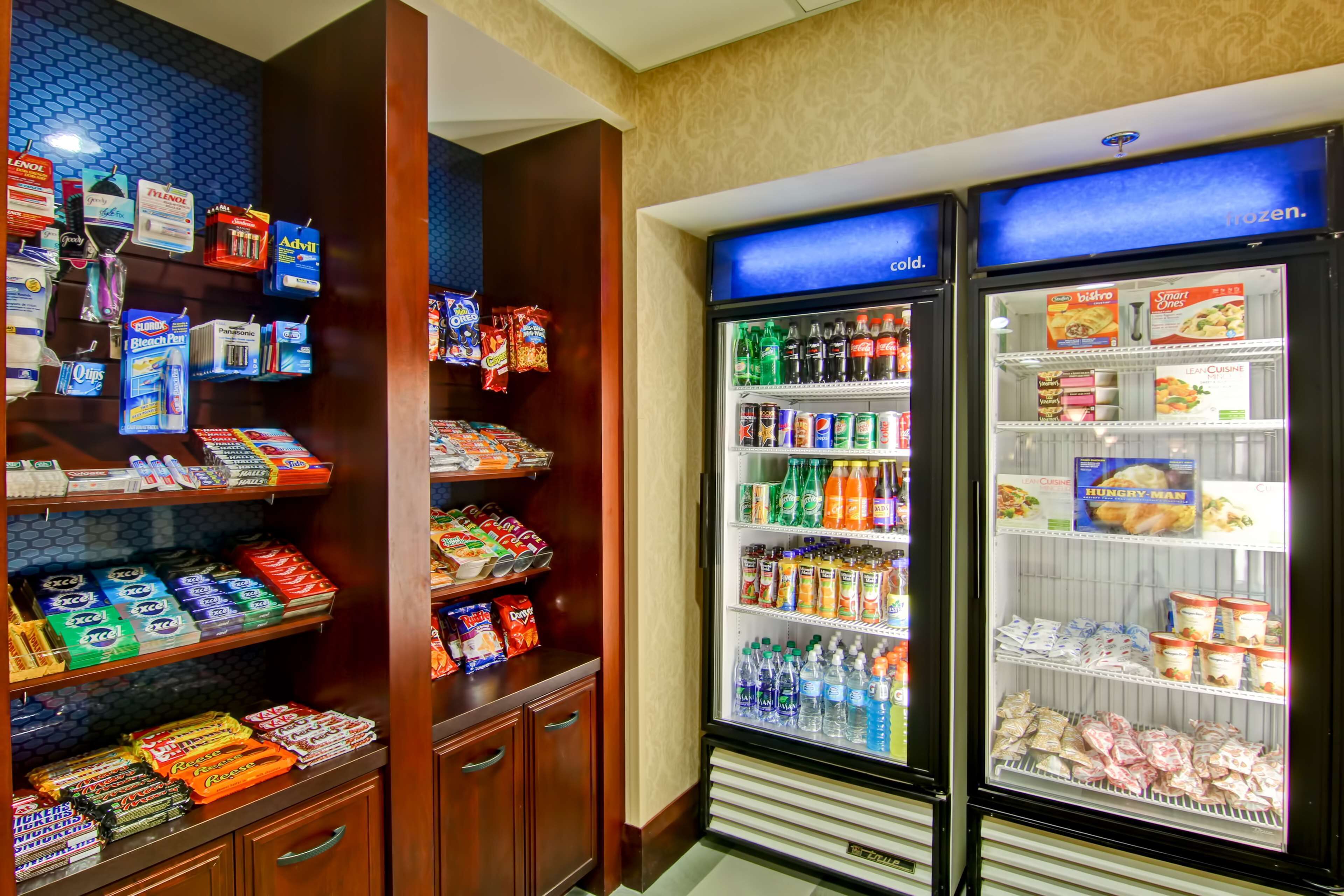 Una máquina expendedora llena de refrigerios y bebidas, junto con un refrigerador que exhibe alimentos congelados.
