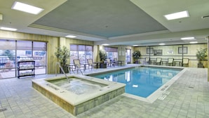 A hotel pool area with a hot tub, lounge chairs, and a view of the outdoors.