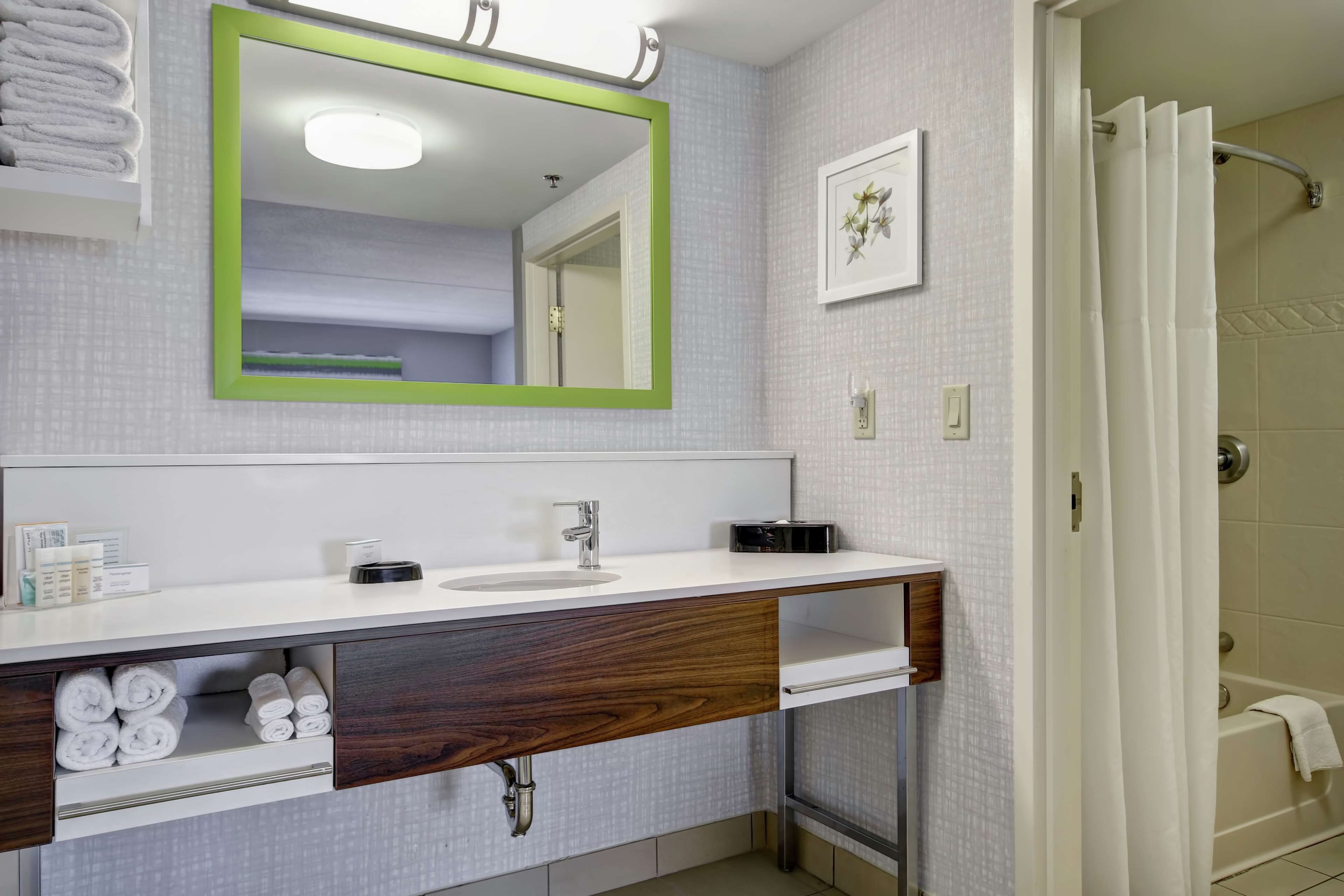 A bathroom with a white sink, a mirror with a green frame, a towel rack, and a shower curtain.