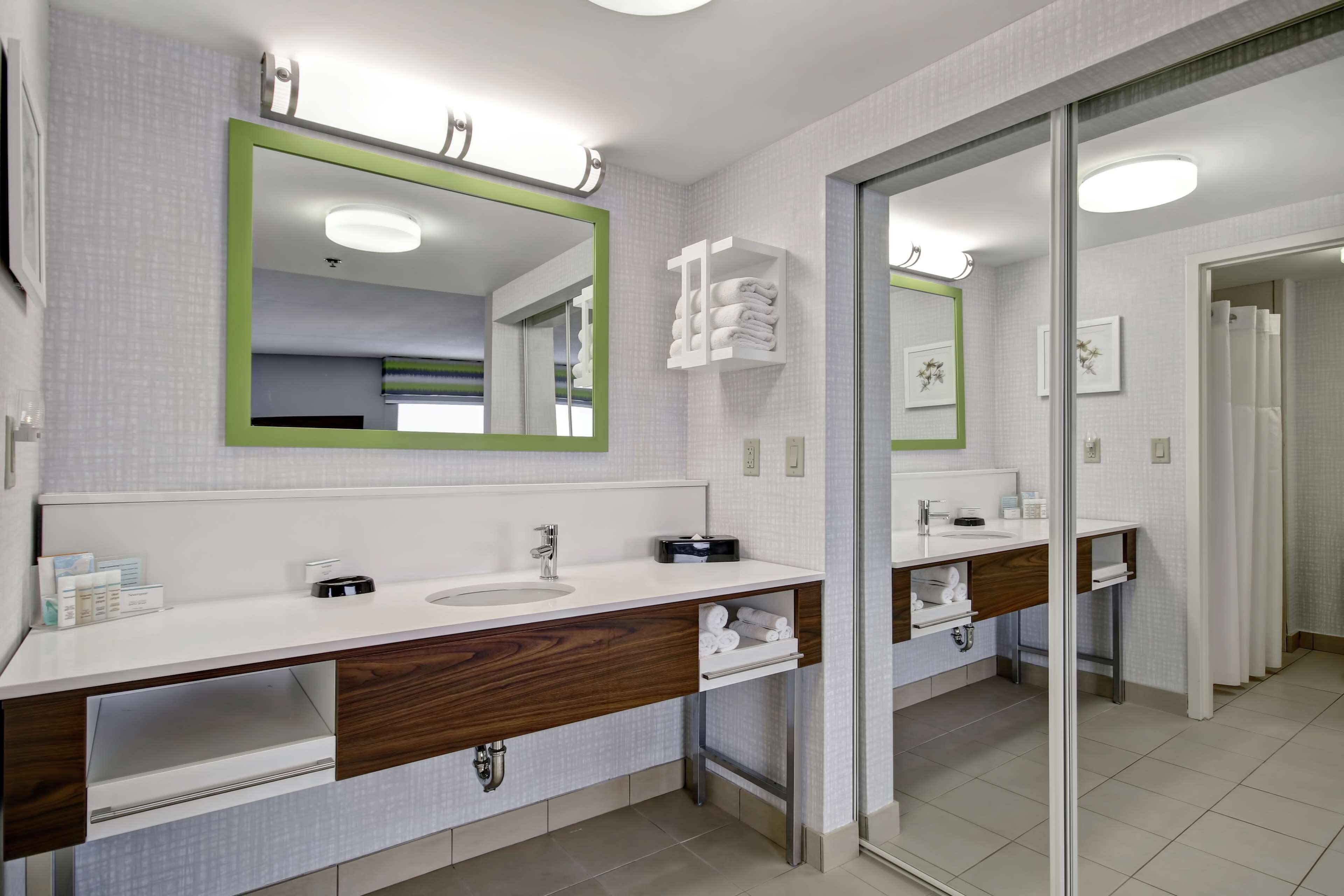 A modern bathroom with two sinks, wooden vanity, and a large mirror with a green frame.