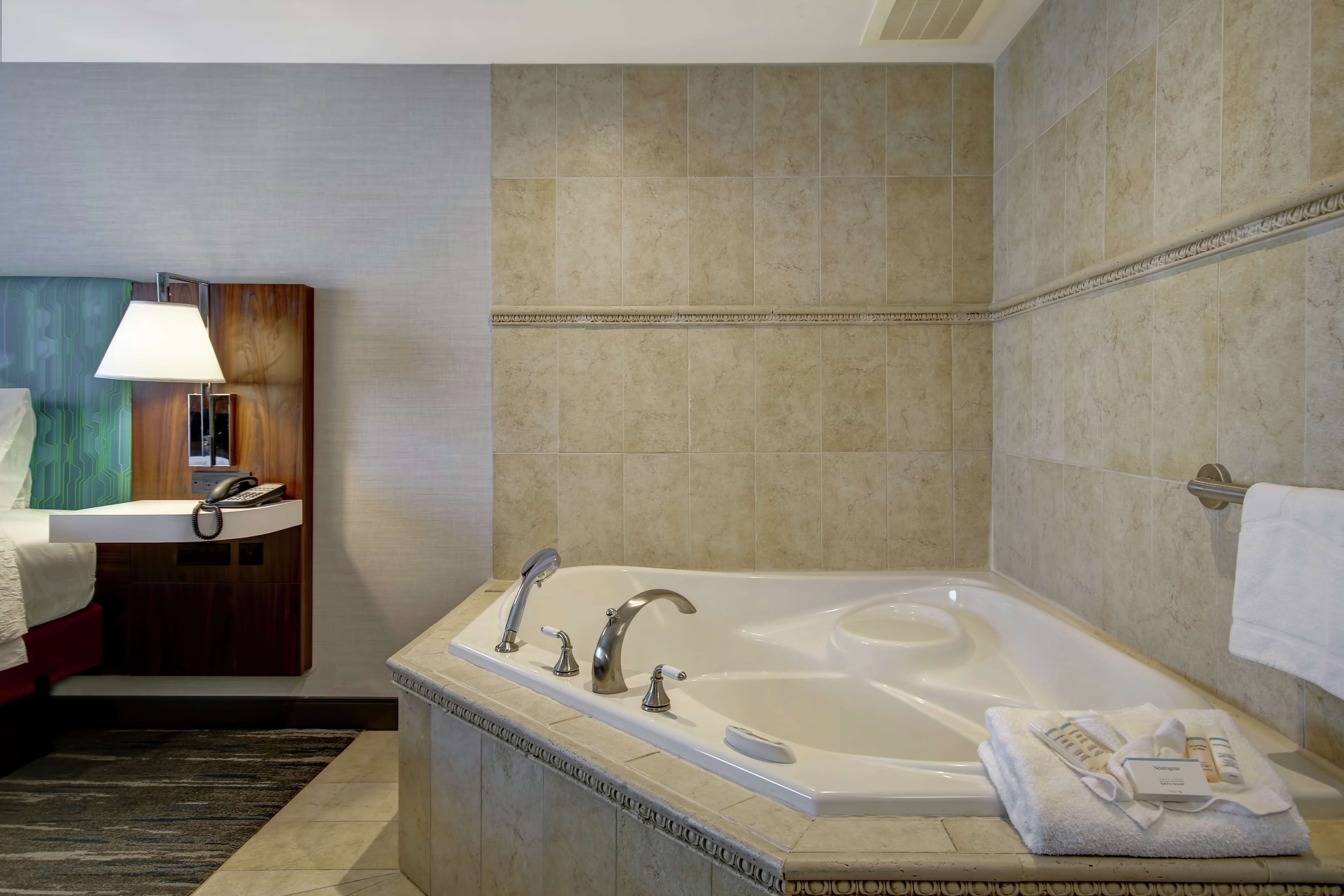 A hotel bathroom with a bathtub, a sink with a mirror, a telephone, and a towel rack.