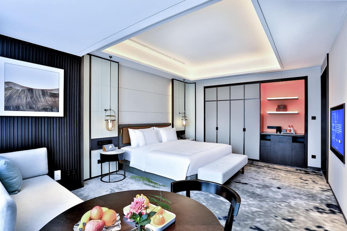 Una habitación de hotel moderna con una cama grande, un escritorio, una zona de estar y una kitchenette.