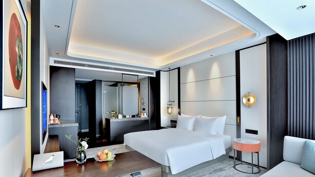 A modern hotel room with a large bed, a desk with a laptop, a bedside table with a vase, and a round table. - Yindu Hotel Yiwu (Jinhua)
