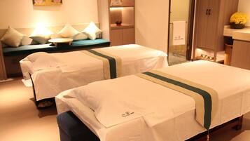 Two single beds with white linens and a green stripe, a small table, and a bench in a minimalist room.