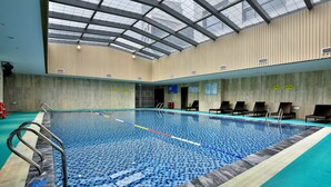 An indoor swimming pool with clear lane markings, a metal ladder, and lounge chairs along the side. - Yindu Hotel Yiwu (Jinhua)