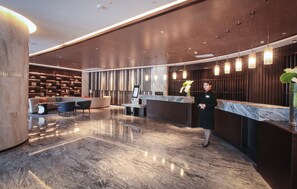 Un área de recepción moderna con suelo de mármol, una mesa de recepción y un espacio de espera con sillas.
