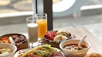 Un bufé de desayuno con diversos platos, como waffles, tortillas y pastelería, servido en una mesa de madera con vista a la calle.