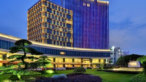 A modern hotel with a prominent vertical design, a well-maintained garden, and a clear sky. - Yindu Hotel Yiwu (Jinhua)