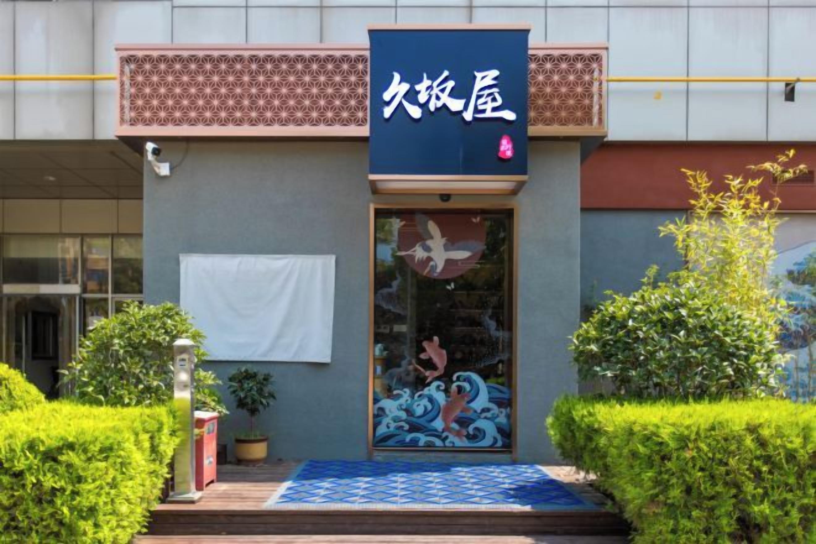 A building with a traditional Japanese entrance, a blue sign with white characters, and a small step leading to the door.