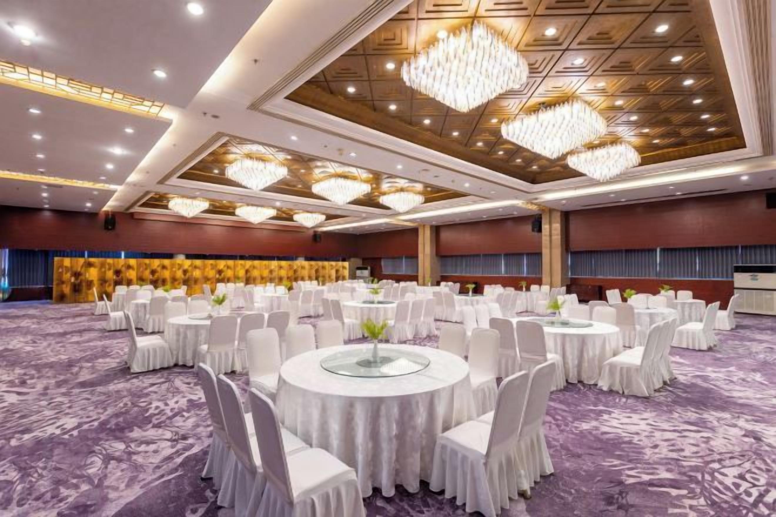 A banquet hall with round tables and chairs, a patterned carpet, and a chandelier.