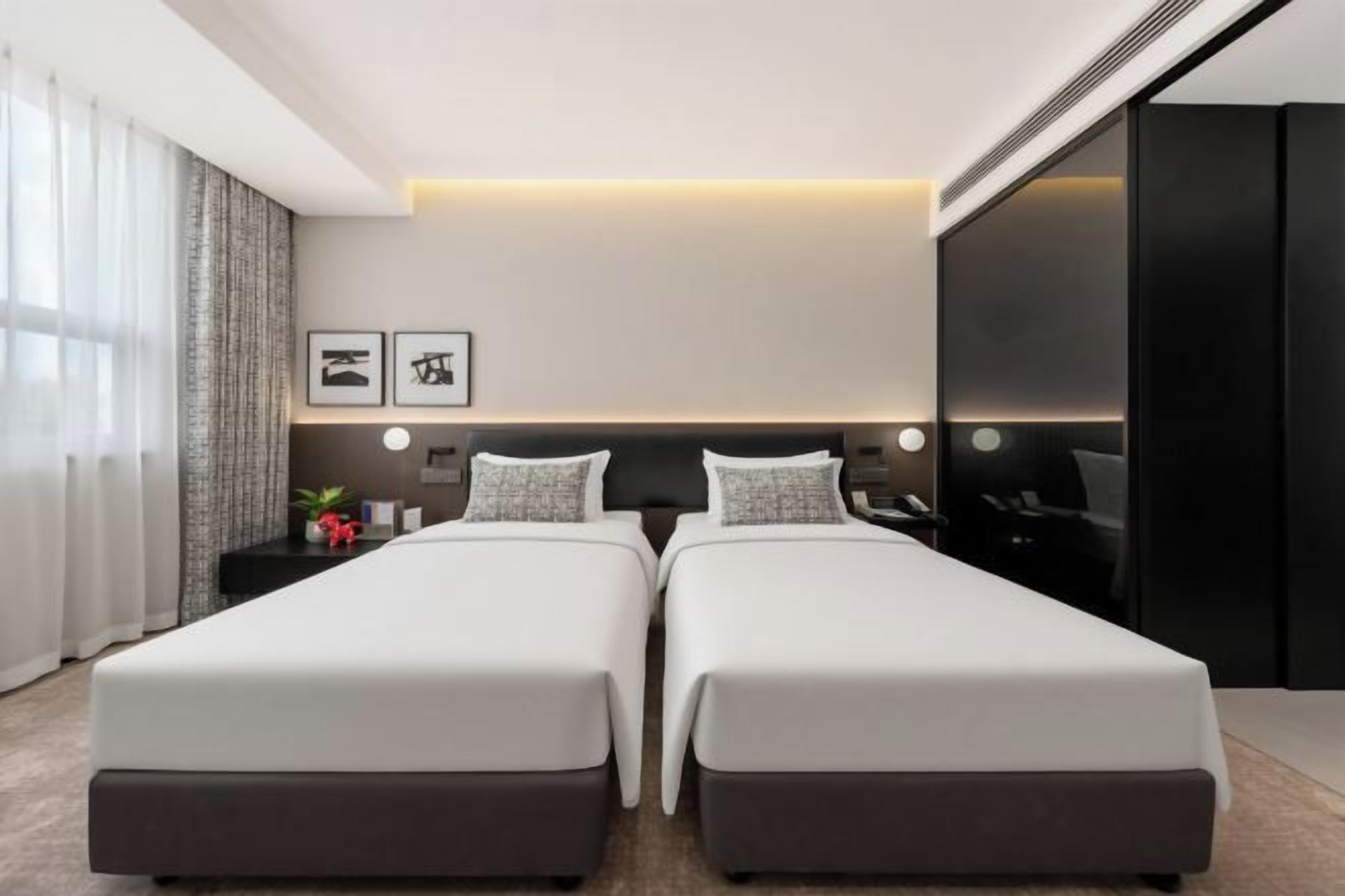 A modern hotel room with two beds, a desk, and a large window with curtains.