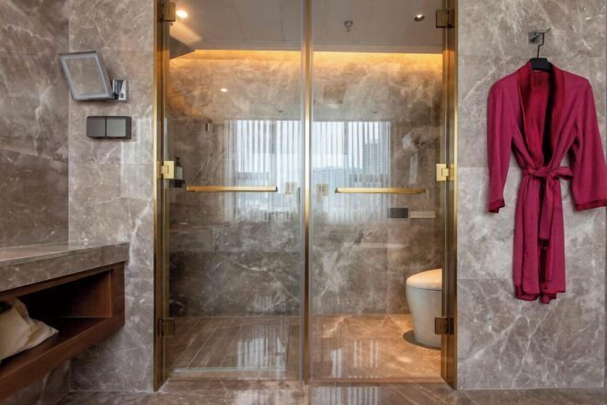 Un baño moderno con cabina de ducha de vidrio, paredes de mármol y una bata roja colgada en la pared.