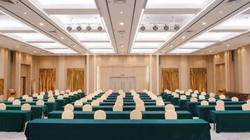 Sala de conferência com fileiras de mesas e cadeiras, um palanque e uma porta ao centro.