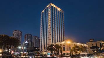 Un edificio de gran altura con diseño moderno, situado en un entorno urbano con otros edificios y una calle concurrida.