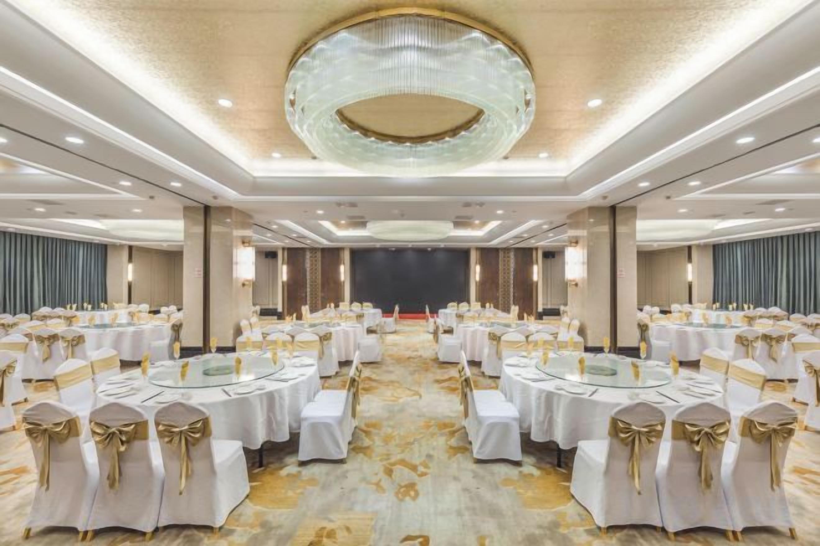 A banquet hall with round tables, white tablecloths, and gold sashes.