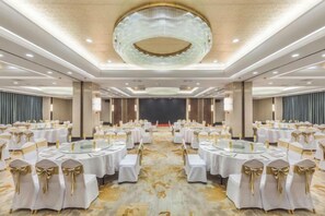 A banquet hall with round tables, white tablecloths, and gold sashes. - XINDU INTERNATIONAL HOTEL (Taizhou)