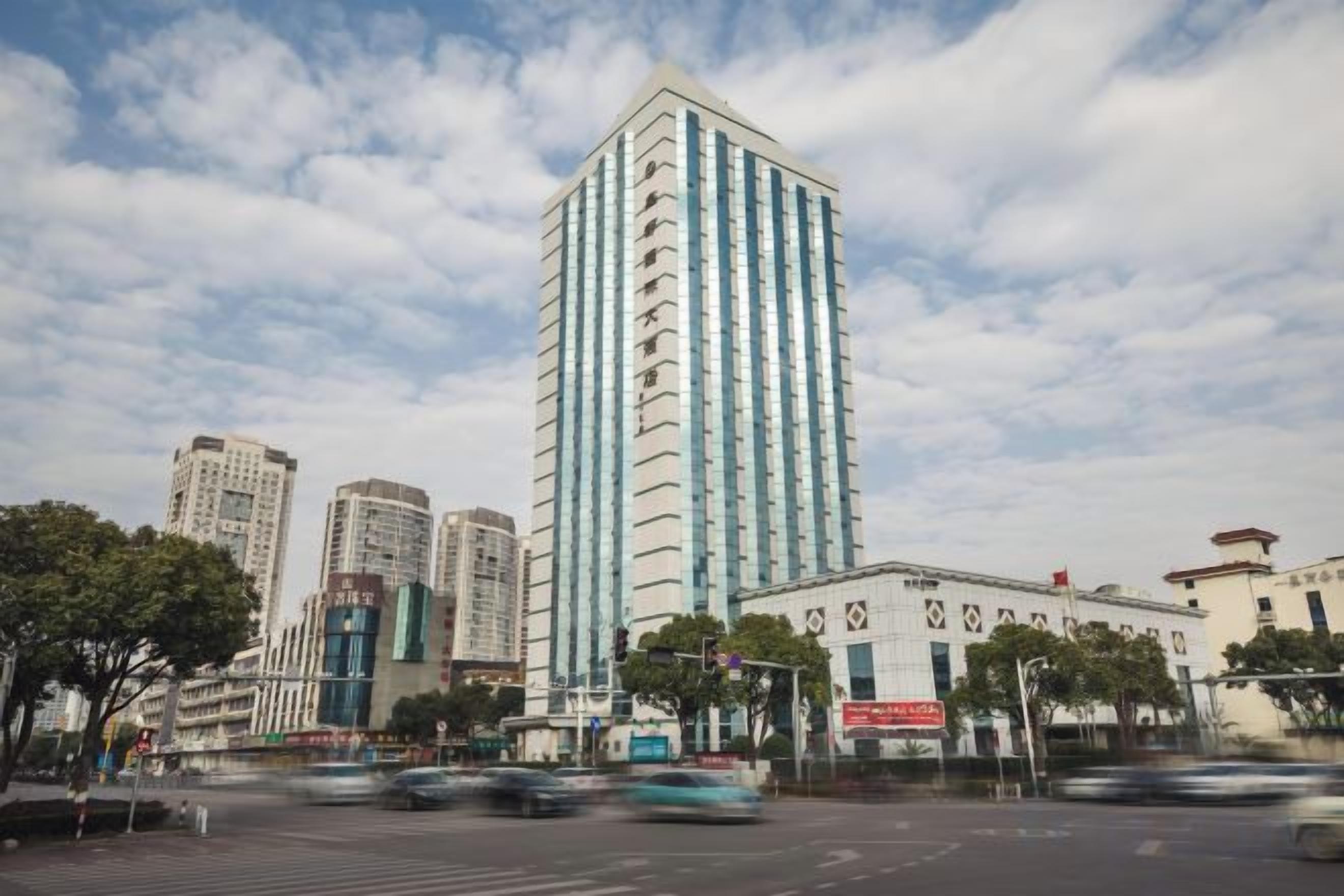 Un edificio moderno de gran altura, rodeado de otros edificios altos y una calle concurrida con vehículos en movimiento.