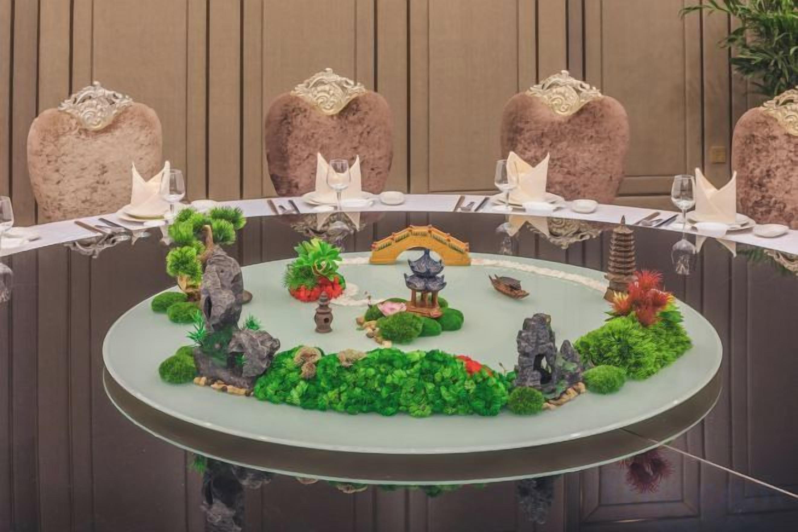 A round table with a decorative centerpiece featuring a miniature landscape with rocks, plants, and a pagoda.