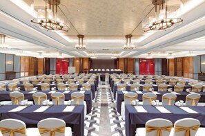 A conference room with rows of tables and chairs, a stage at the front, and a modern chandelier. - XINDU INTERNATIONAL HOTEL (Taizhou)