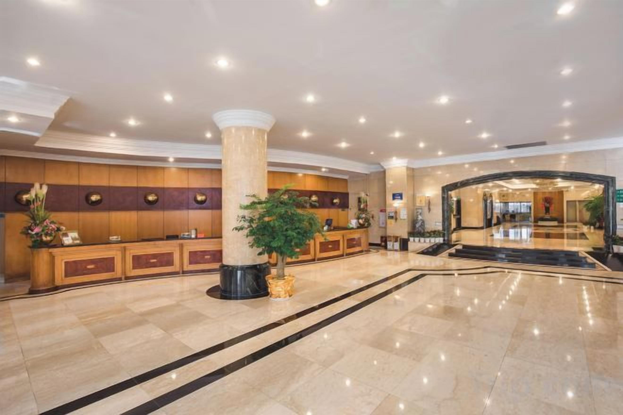 Un hall d’hôtel avec un comptoir d’accueil, une grande colonne et une plante.
