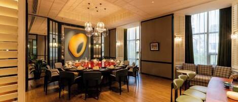 A dining area with a round table, chairs, and a chandelier. There is a sofa and a bench in the background.