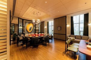 Un comedor con una mesa redonda, sillas y un candelabro. Se observa un sofá y un banco al fondo.