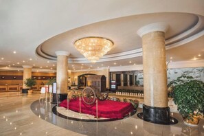 A lobby with a grand chandelier, marble columns, a red carpet, and a vintage carriage. - XINDU INTERNATIONAL HOTEL (Taizhou)
