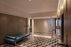 A hotel room with a bench, a patterned floor, a door, and a wall with a light switch. - XINDU INTERNATIONAL HOTEL (Taizhou)