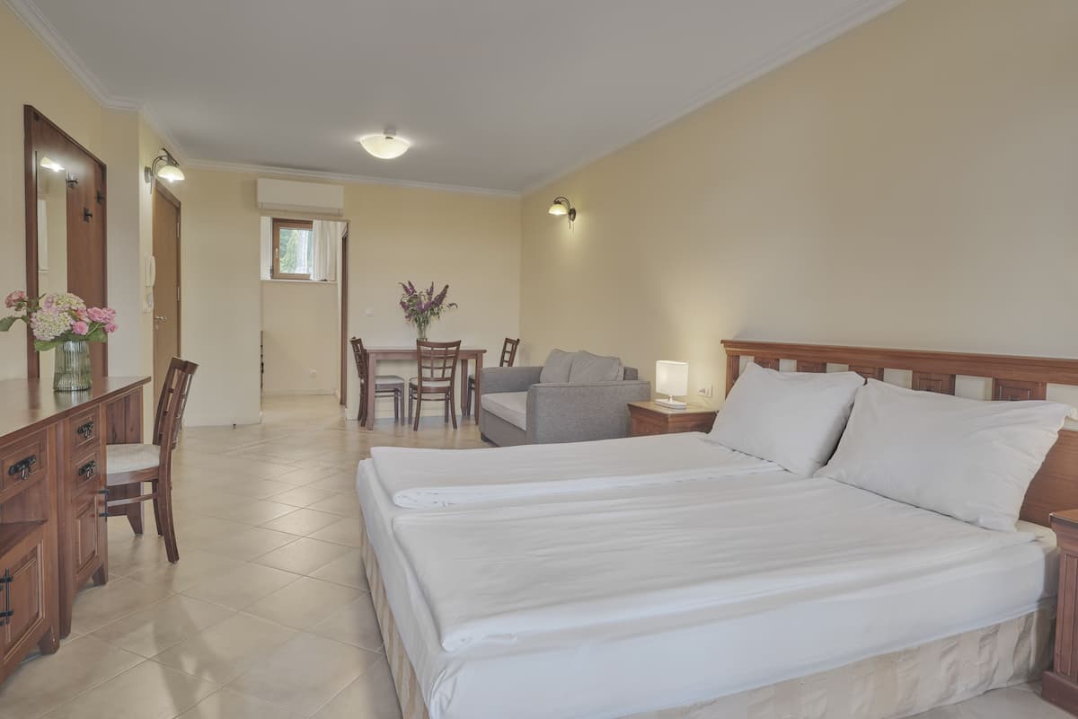 A hotel room with a large bed, a desk with a chair, a dining table with chairs, and a sofa.
