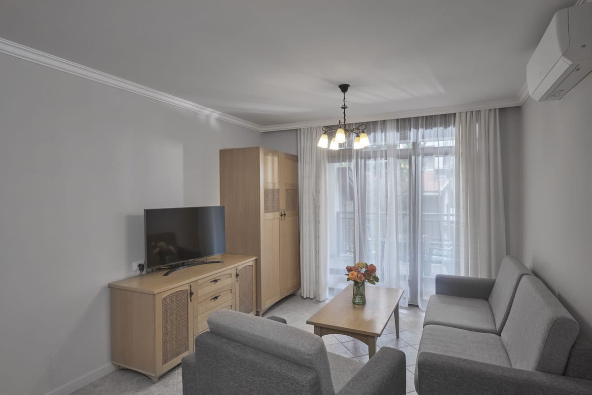 A modern living room with a flat-screen TV, a wooden cabinet, a sofa, a coffee table, and a chandelier.