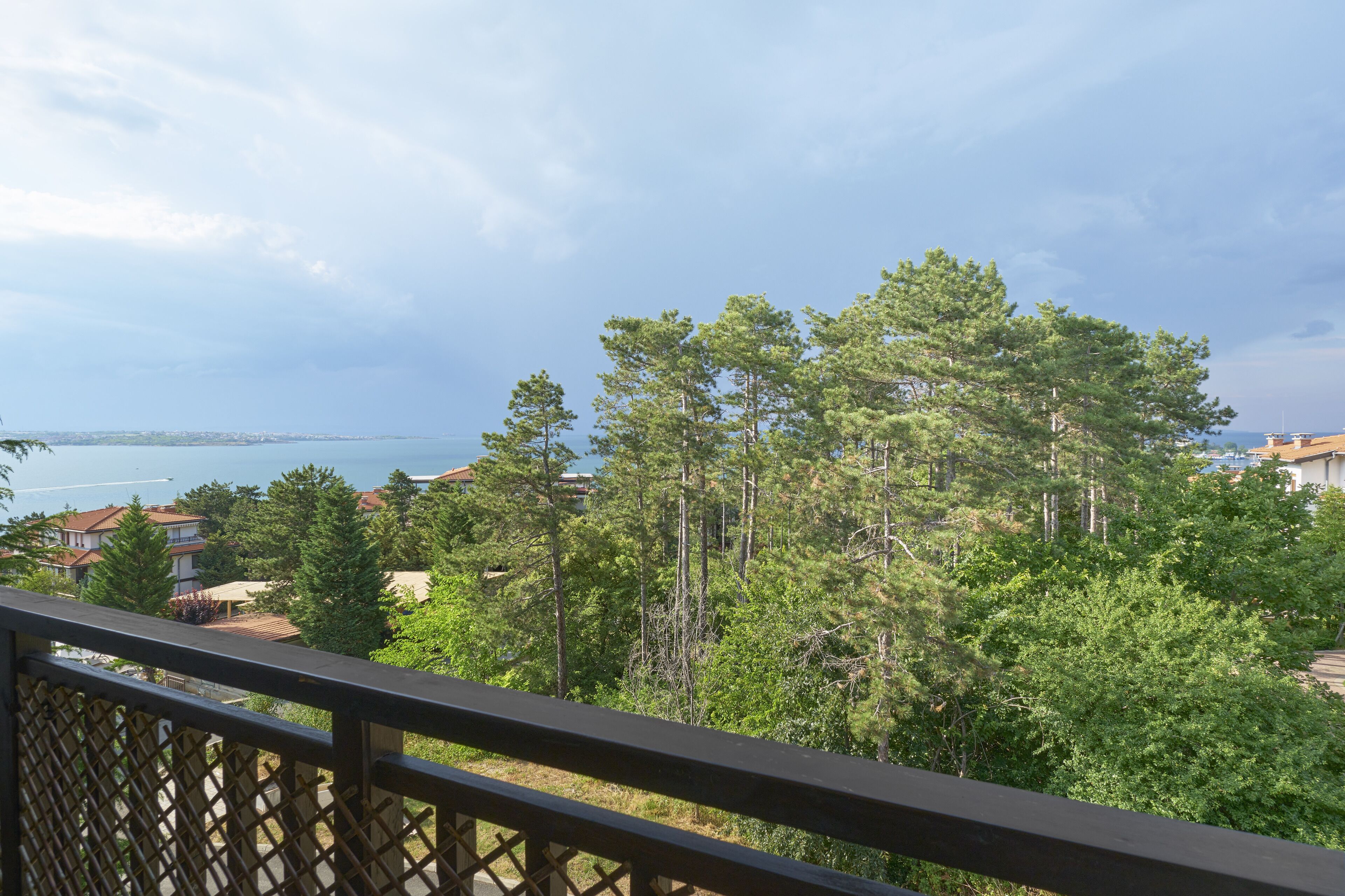 En balkon med udsigt over kystlandskab, frodig vegetation og en bro i det fjerne.