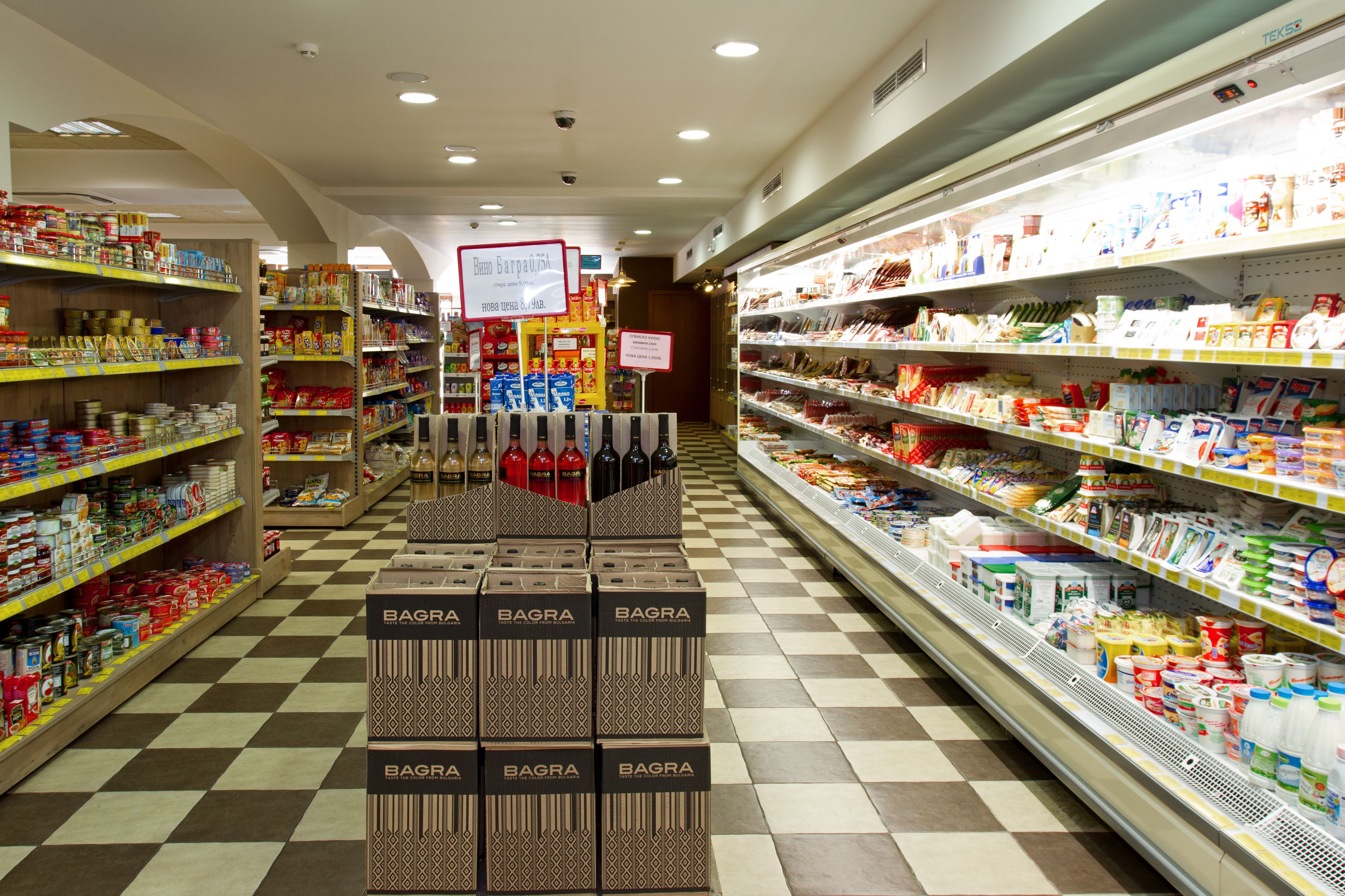 Un pasillo de un supermercado con estantes repletos de diversos productos, incluyendo un expositor de cajas Bagra en el centro.