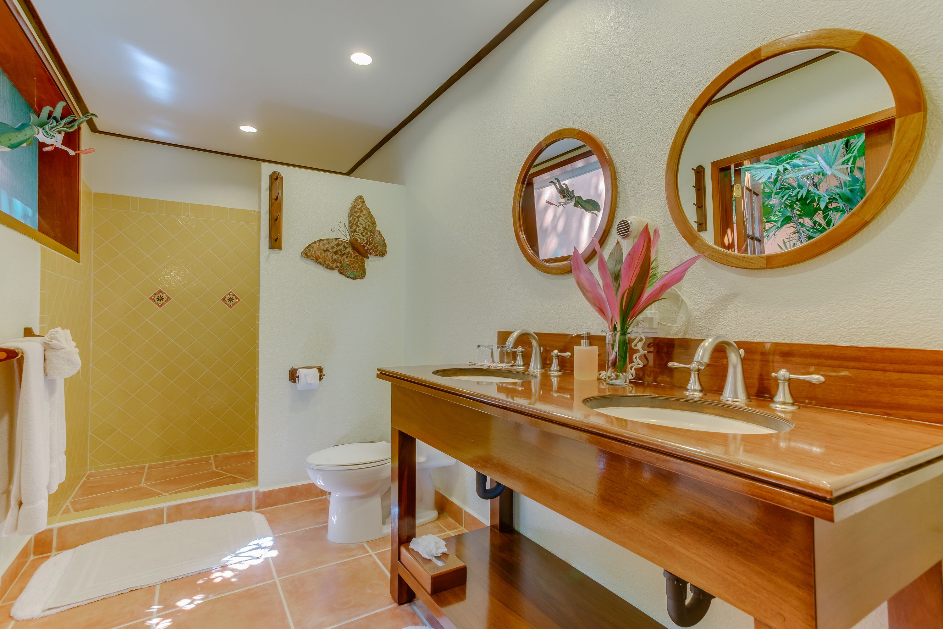 Un baño con dos lavamanos, una ducha y un inodoro. Se observan mariposas decorativas y un espejo en la pared.