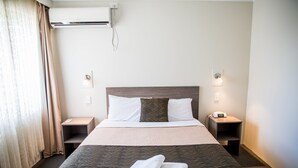 Una camera d'albergo con un letto grande, due comodini, un condizionatore d'aria e una finestra con tende.