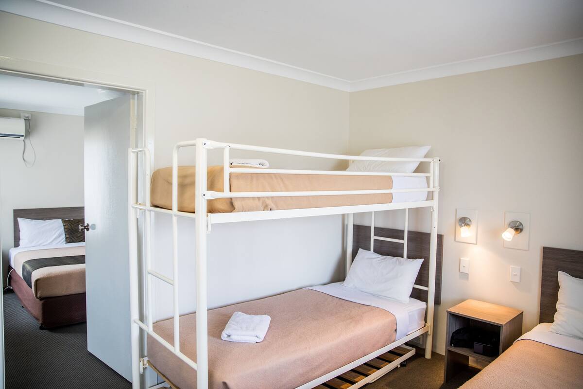 Habitación con literas, suelo de madera, mesita de noche y lámpara fijada a la pared.