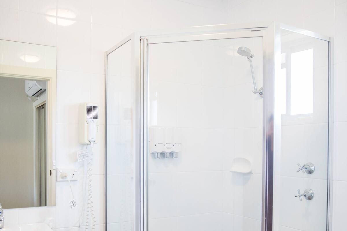 Un baño moderno con ducha envuelta en vidrio, lavamanos blanco y espejo.