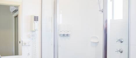 Un baño moderno con ducha envuelta en vidrio, lavamanos blanco y espejo.