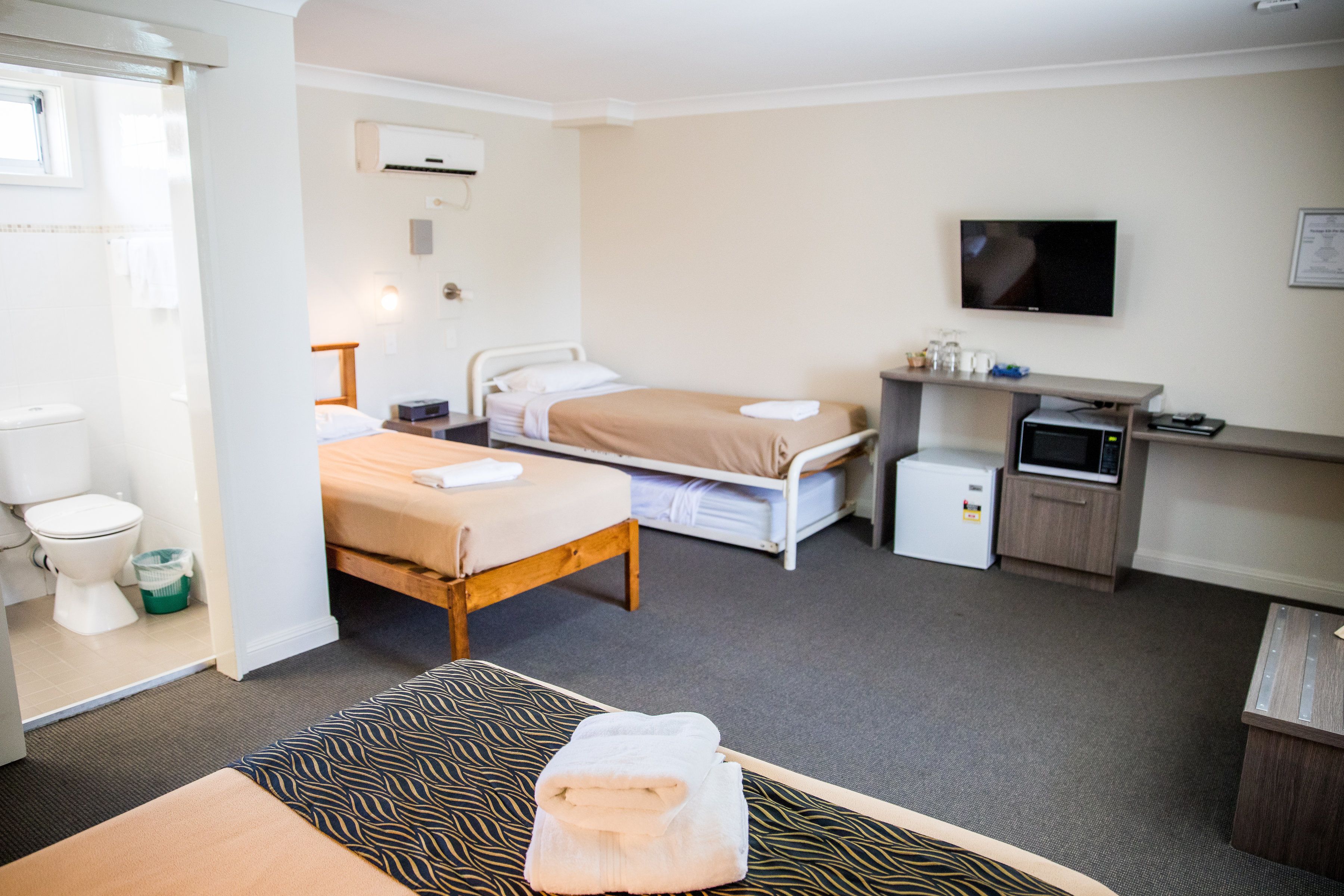 A hotel room with a bed, bedside table, a small desk with a computer, a microwave, and a TV.