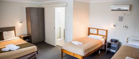 Habitación de hotel con dos camas, un armario, una mesita de noche, un aire acondicionado y una silla.