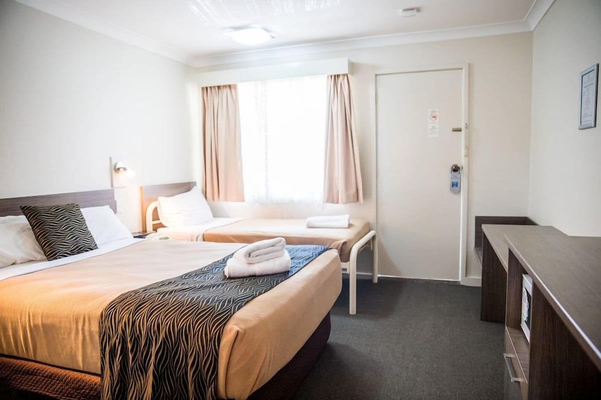 Quarto de hotel com duas camas, uma escrivaninha e uma porta.