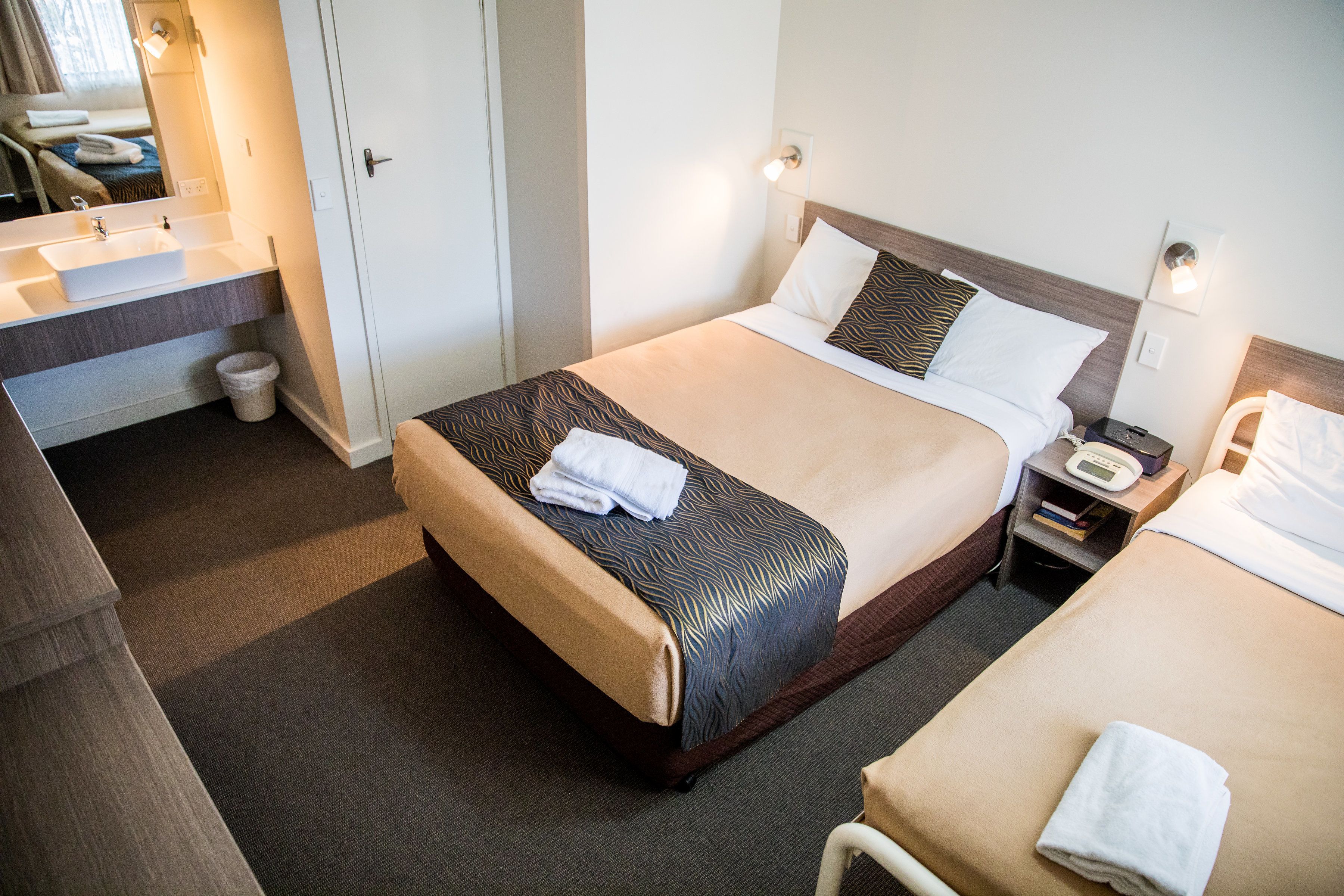 A hotel room with a bed, bedside tables, a desk with a sink, and a mirror.