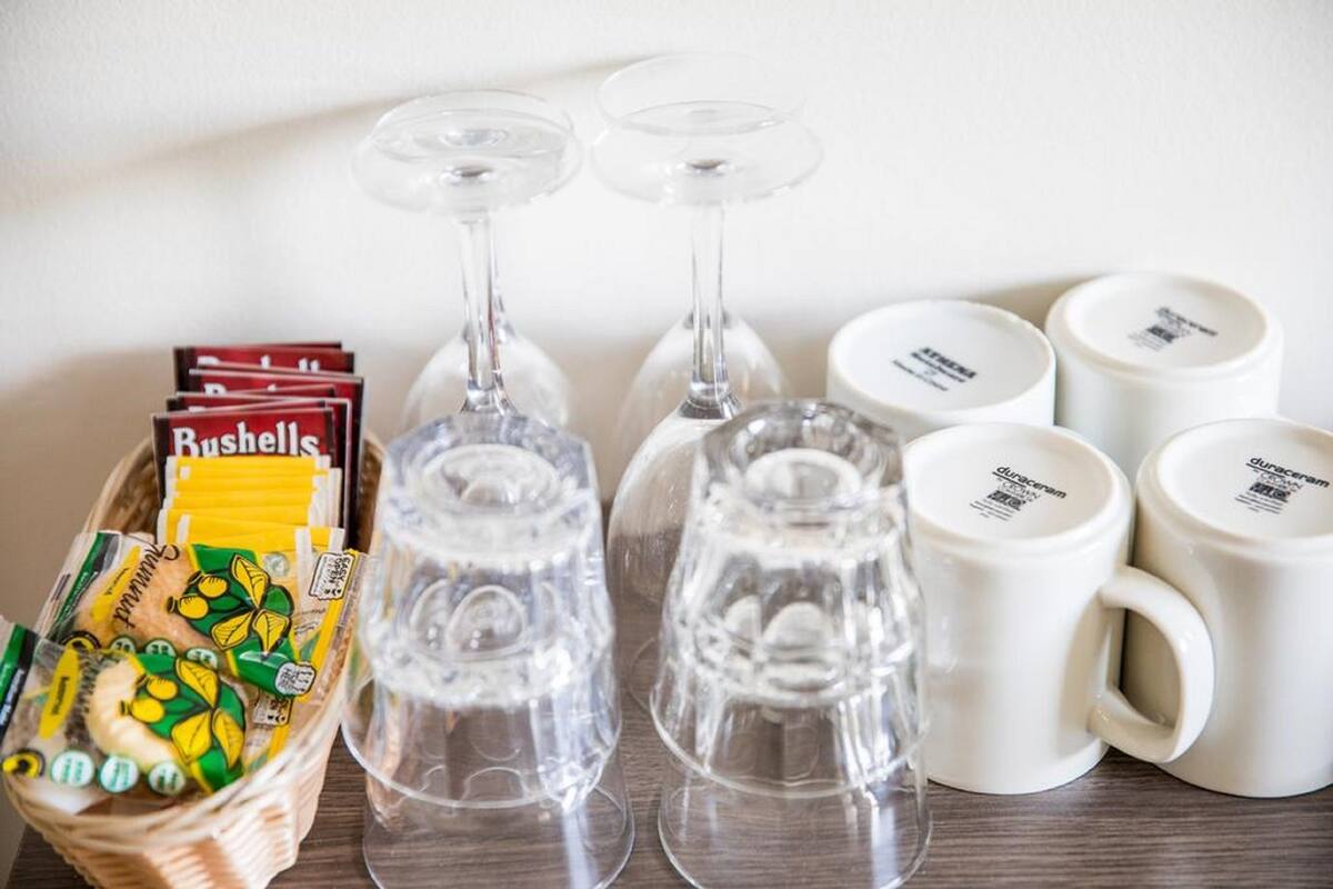 Una mesa con copas de vino, una cesta de aperitivos y tazas blancas.