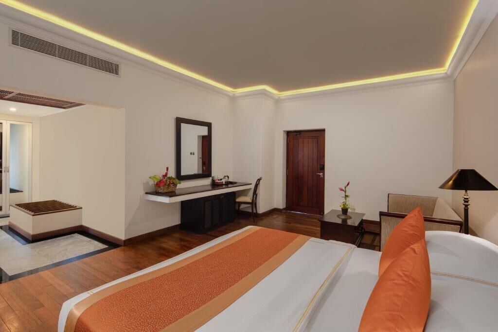 A hotel room with a bed, a desk, a chair, a mirror, and a lamp.