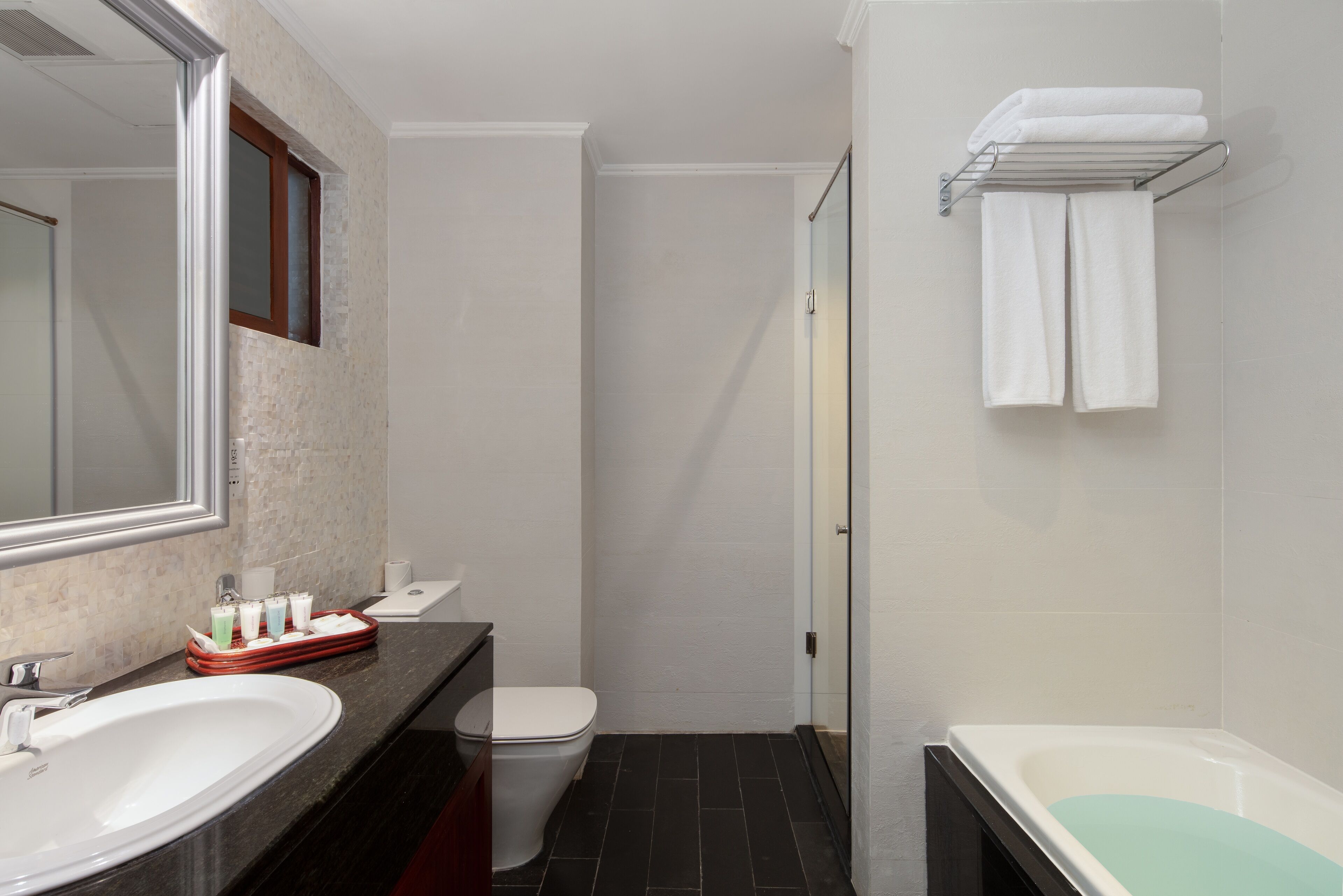 A modern bathroom with a large mirror, a white sink, a toilet, and a bathtub.