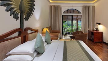 Quarto de hotel com uma cama, um espaço de estar com mesa e cadeiras, uma luminária e vista para o exterior pela janela.