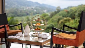 Una mesa dispuesta para una ceremonia de té, con un soporte de tres niveles, dos sillas y vistas a un paisaje verde.