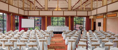 Une salle de conférence avec des rangées de chaises blanches, une scène surmontée d’une table blanche et un grand lustre.