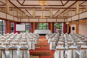 A conference room with rows of white chairs, a stage with a white table, and a large chandelier.